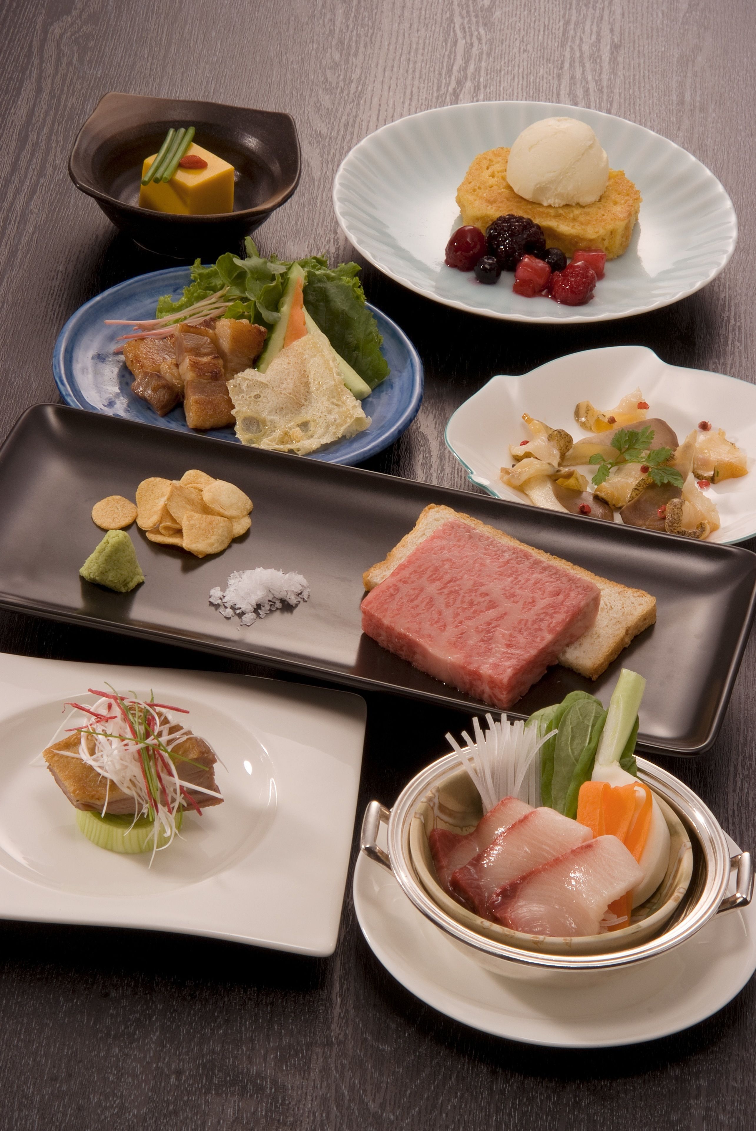 A variety of dishes on a table, including sushi, sashimi, and a dessert with berries.