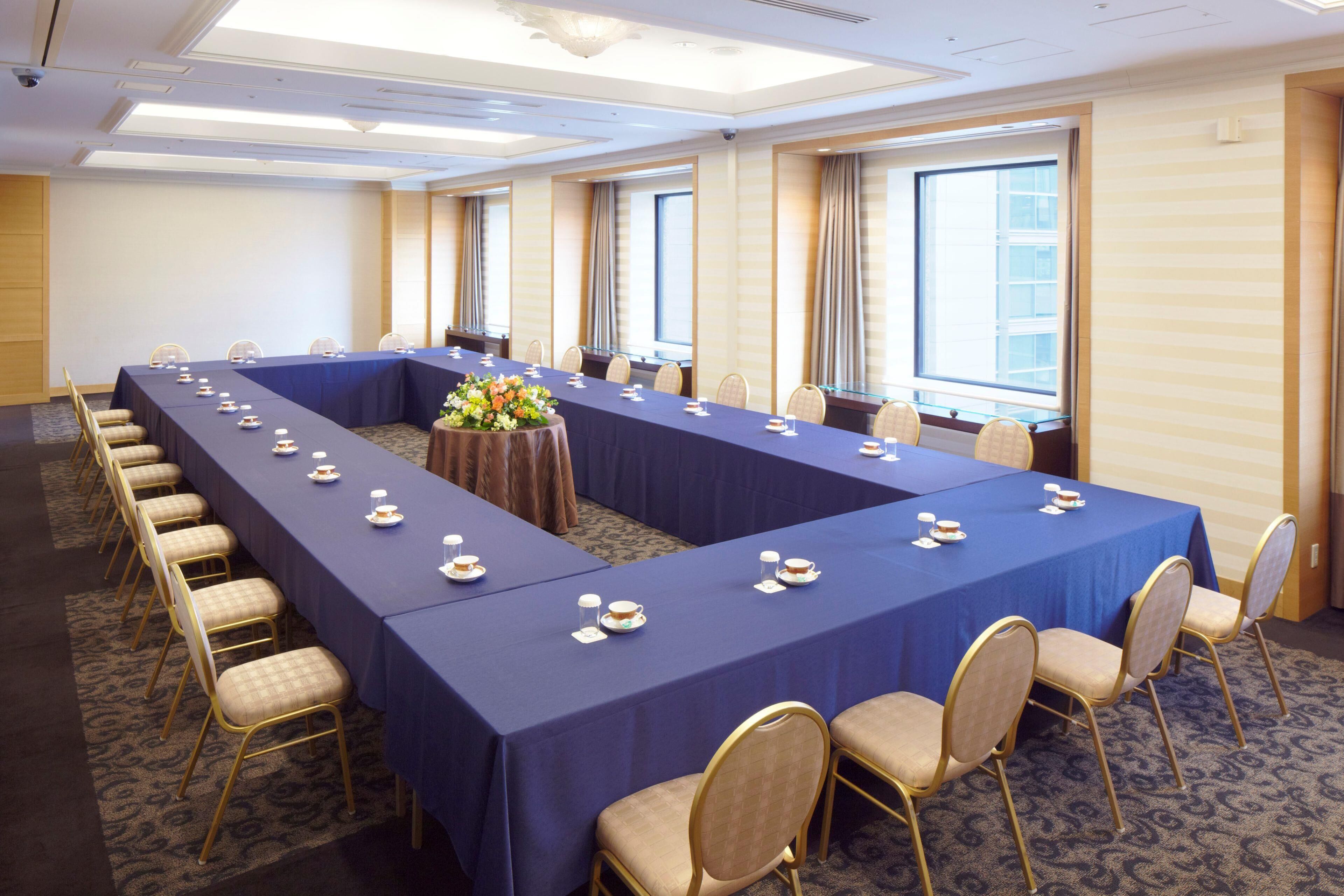 Un salón de conferencias con una larga mesa, sillas y un centro de mesa floral.