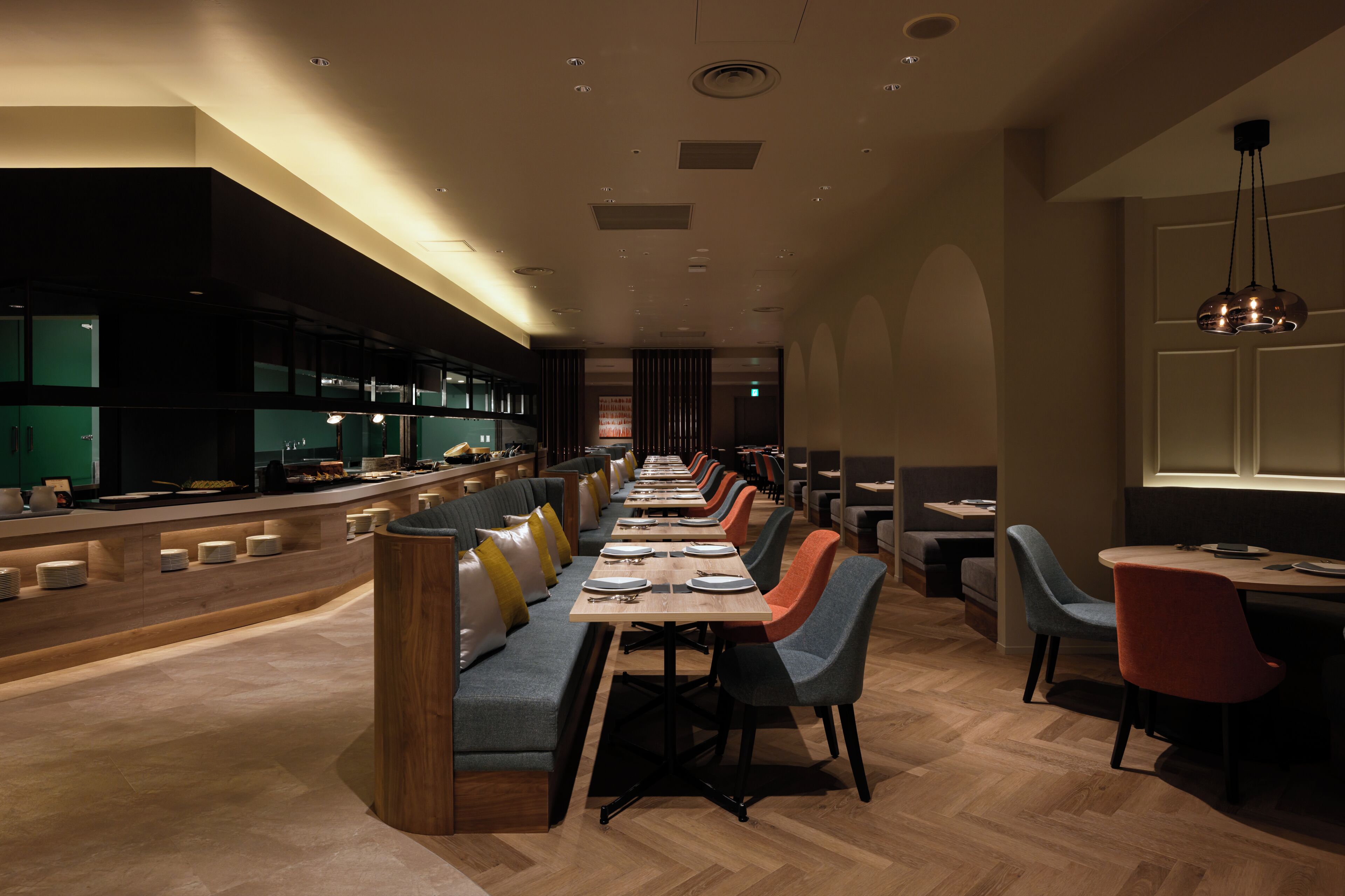 Un restaurante moderno con una barra alargada, varias zonas de estar y una cocina al fondo.