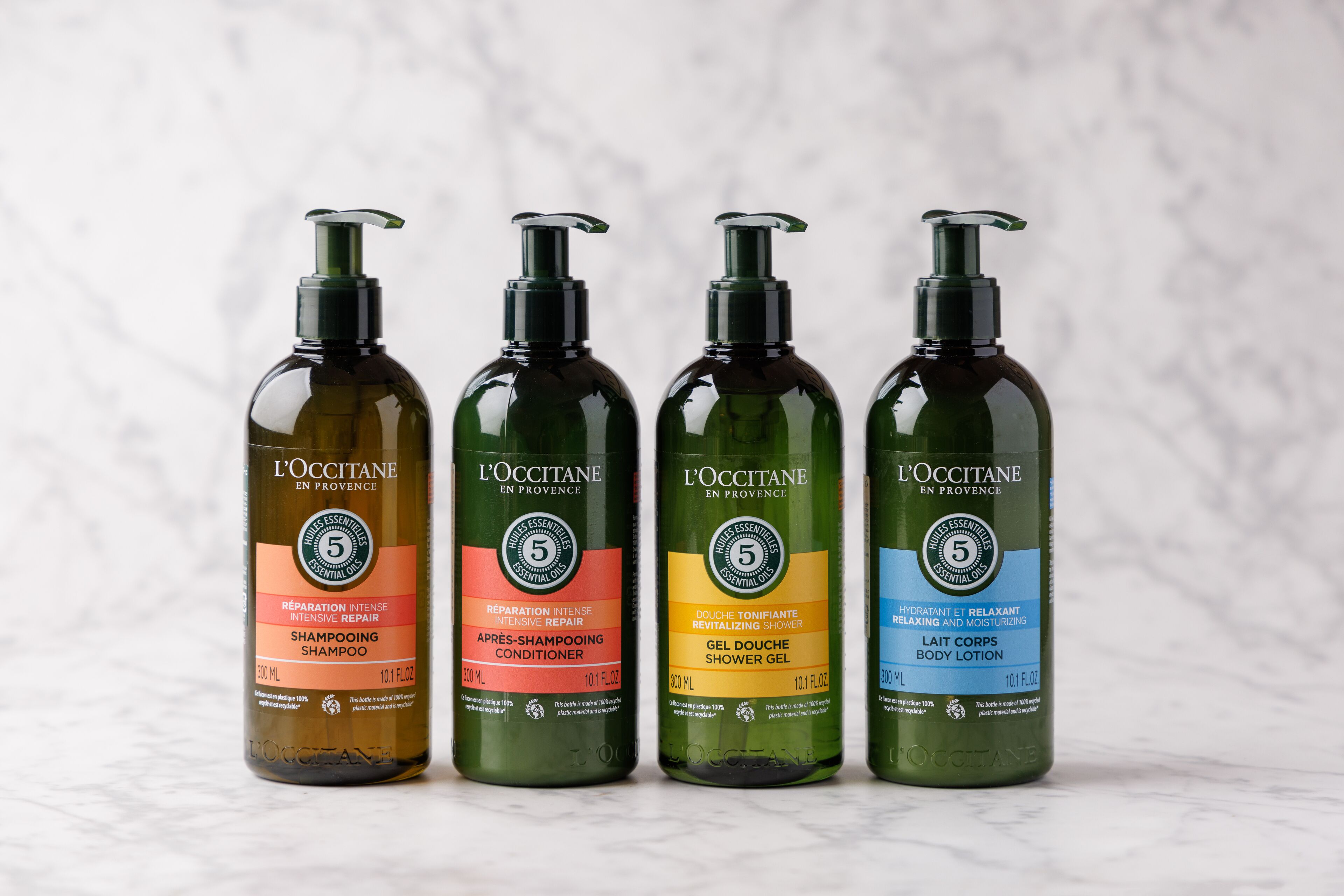 Four bottles of L'OCCITANE products on a marble surface.