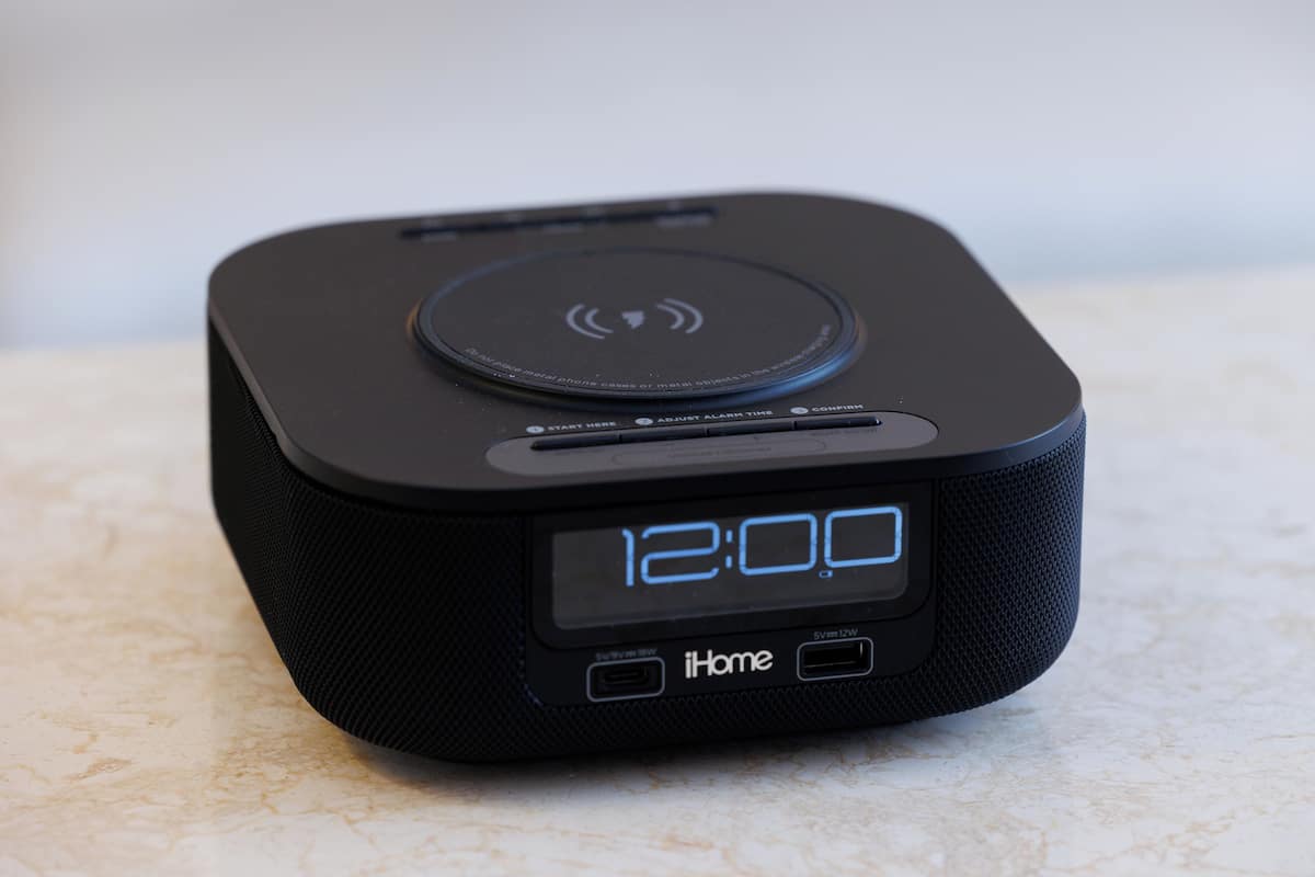 A black iHome speaker with a digital clock displaying 12:00, positioned on a marble surface.