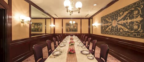 Una larga mesa de banquete dispuesta para un evento formal, con sillas a ambos lados, un candelabro y luces en la pared.