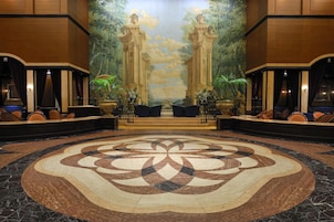 A lobby with a large floral carpet, a mural with columns, and seating areas with plants.
