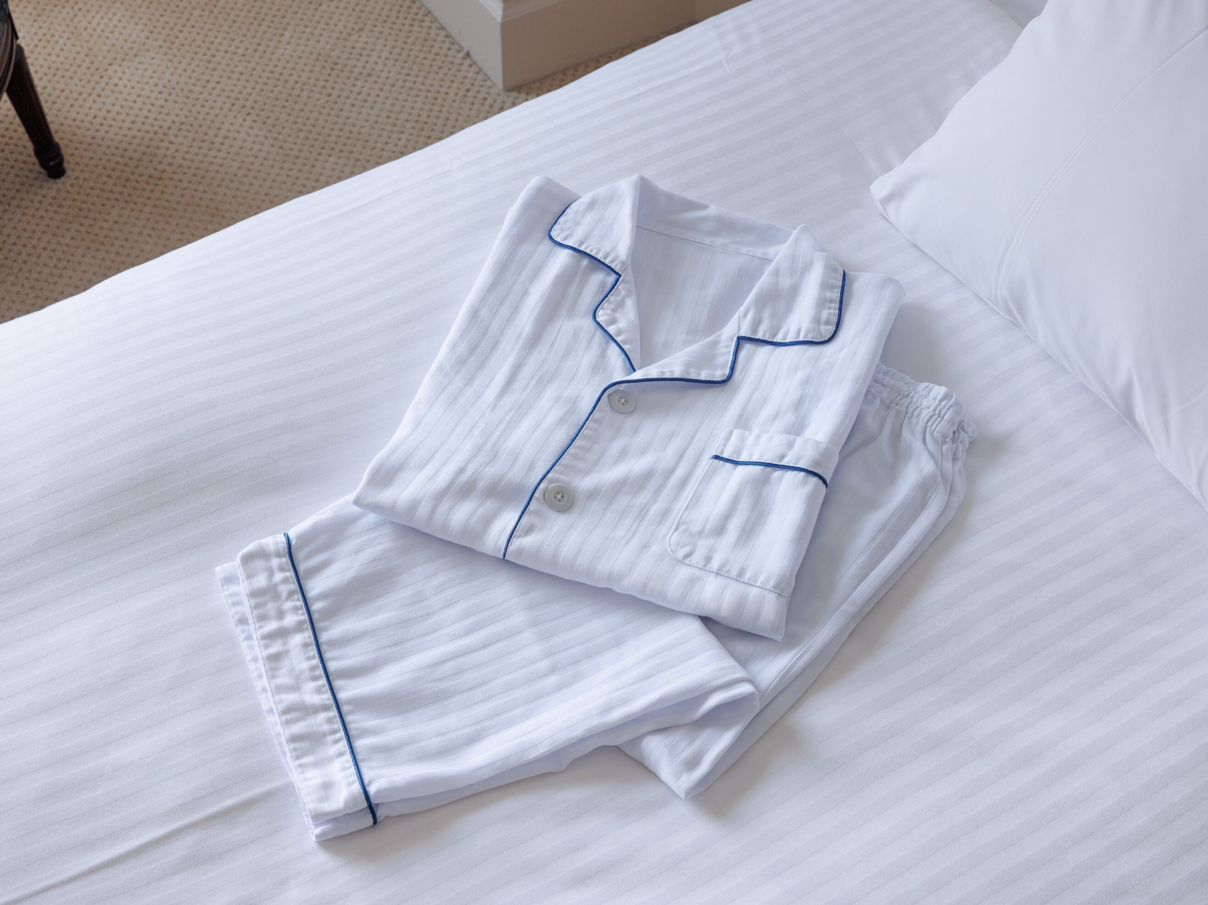 En snyggt bäddad säng med vita sängkläder och ett par blårandiga pyjamasar prydligt vikta ovanpå.