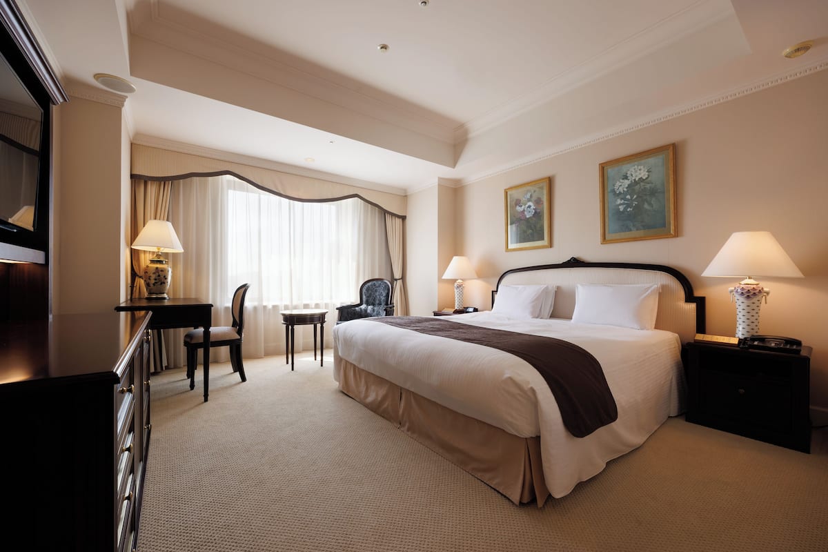 A hotel room with a large bed, a desk with a chair, a small table, and two lamps.