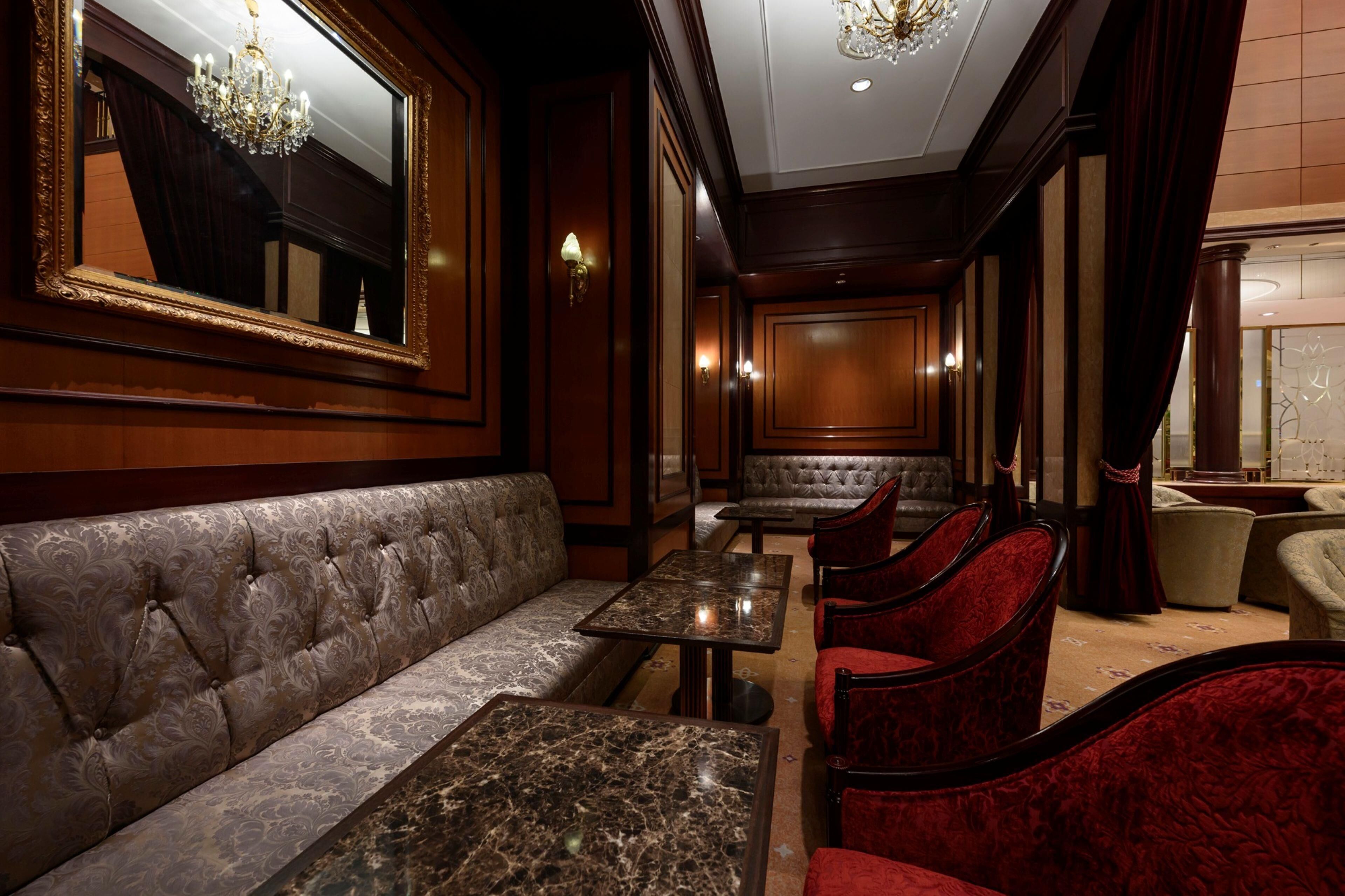 A luxurious interior with a sofa, red velvet chairs, a marble table, and a chandelier.
