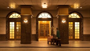 A hotel lobby with a grand entrance, marble columns, and a luggage cart.