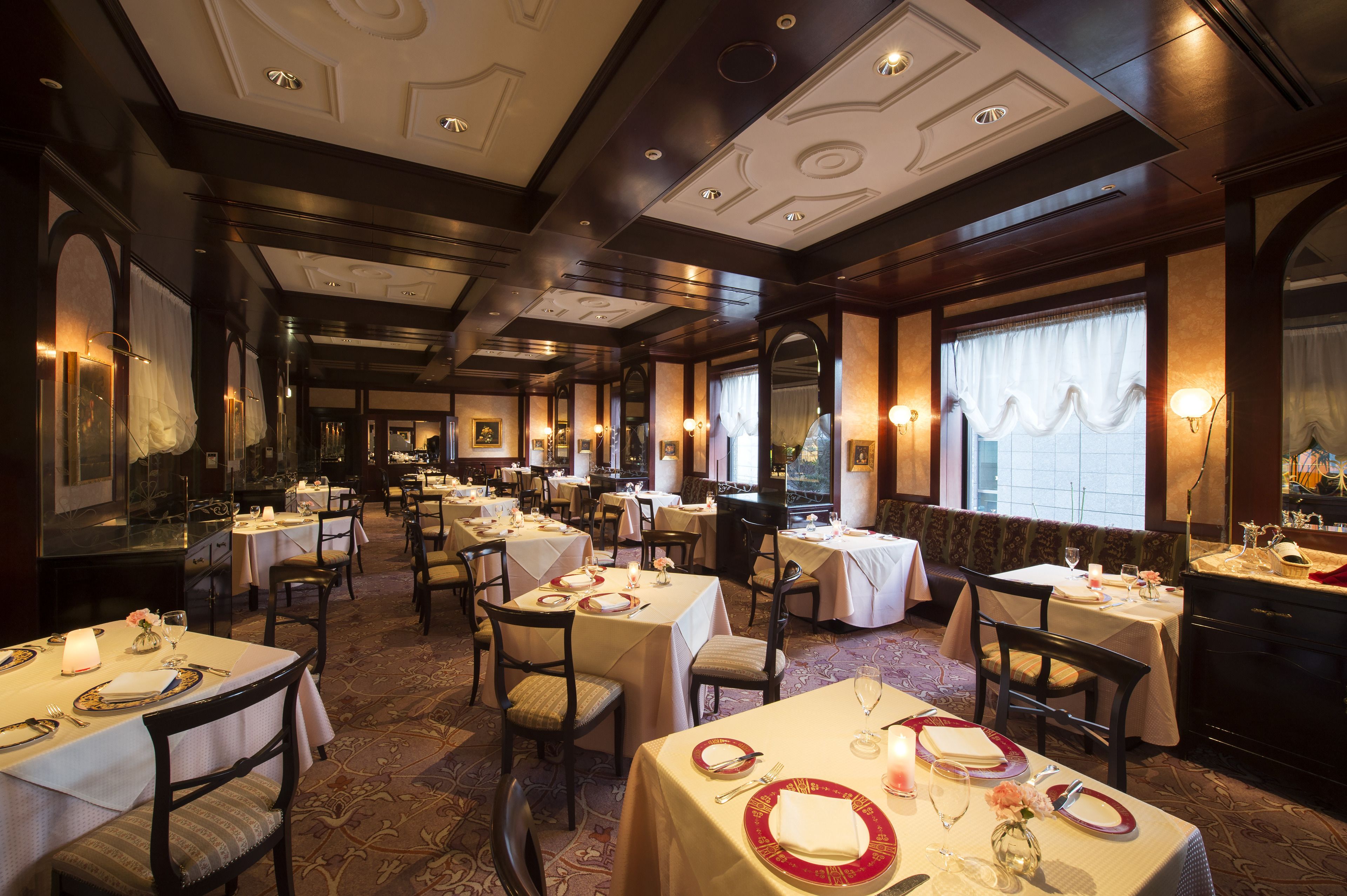 A formal dining area with multiple tables set for service, elegant chandeliers, and classic decor.