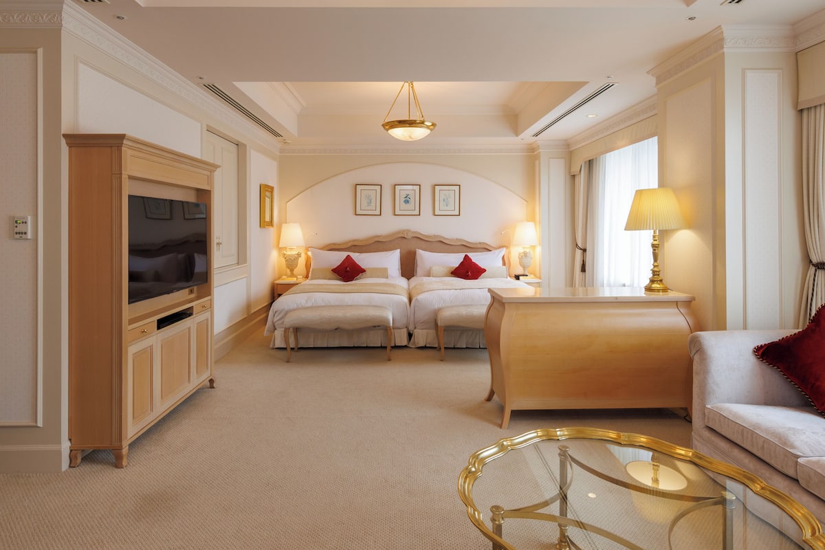 A hotel room with two beds, a TV, a glass coffee table, and a sofa.