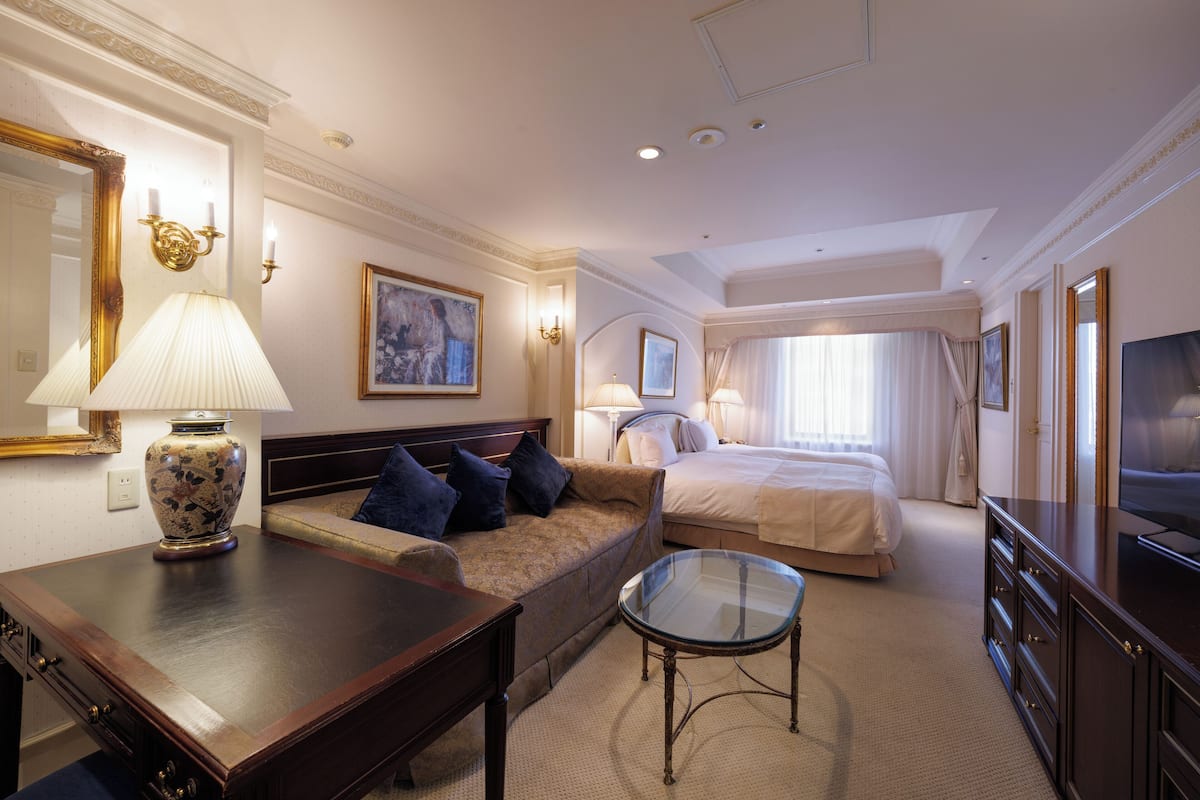 A hotel room with a bed, a sofa, a TV, a lamp, and a mirror.