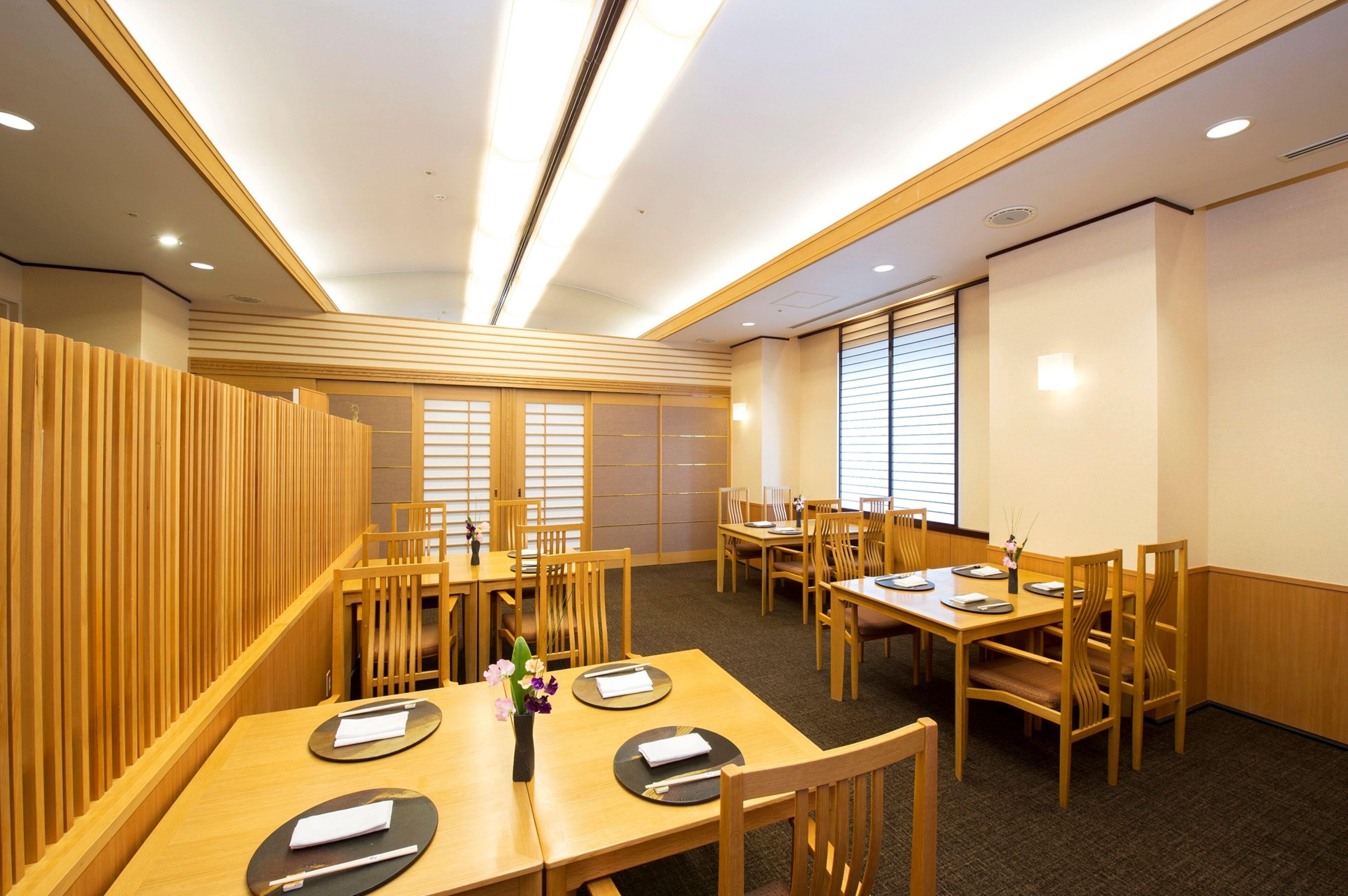 A hotel dining area with wooden furniture, tables set with plates, and a vase with flowers.