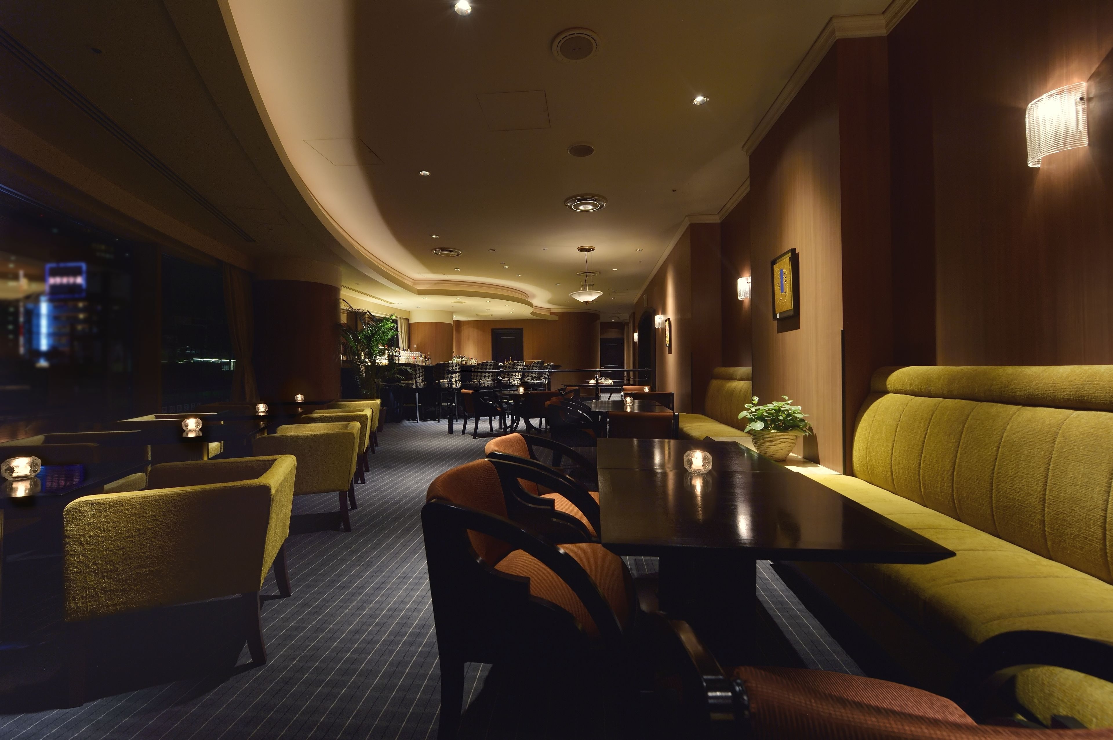 A dimly lit restaurant with yellow upholstered booths and tables, a curved ceiling, and framed pictures on the walls.