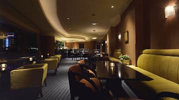 A dimly lit restaurant with yellow upholstered booths and tables, a curved ceiling, and framed pictures on the walls.