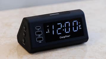 Eine schwarze digitale Uhr mit Anzeige von 12:00 Uhr auf einer Marmoroberfläche, Marke 'ChargeTime'.