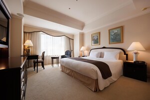 A hotel room with a large bed, a desk, a chair, and two paintings on the wall.