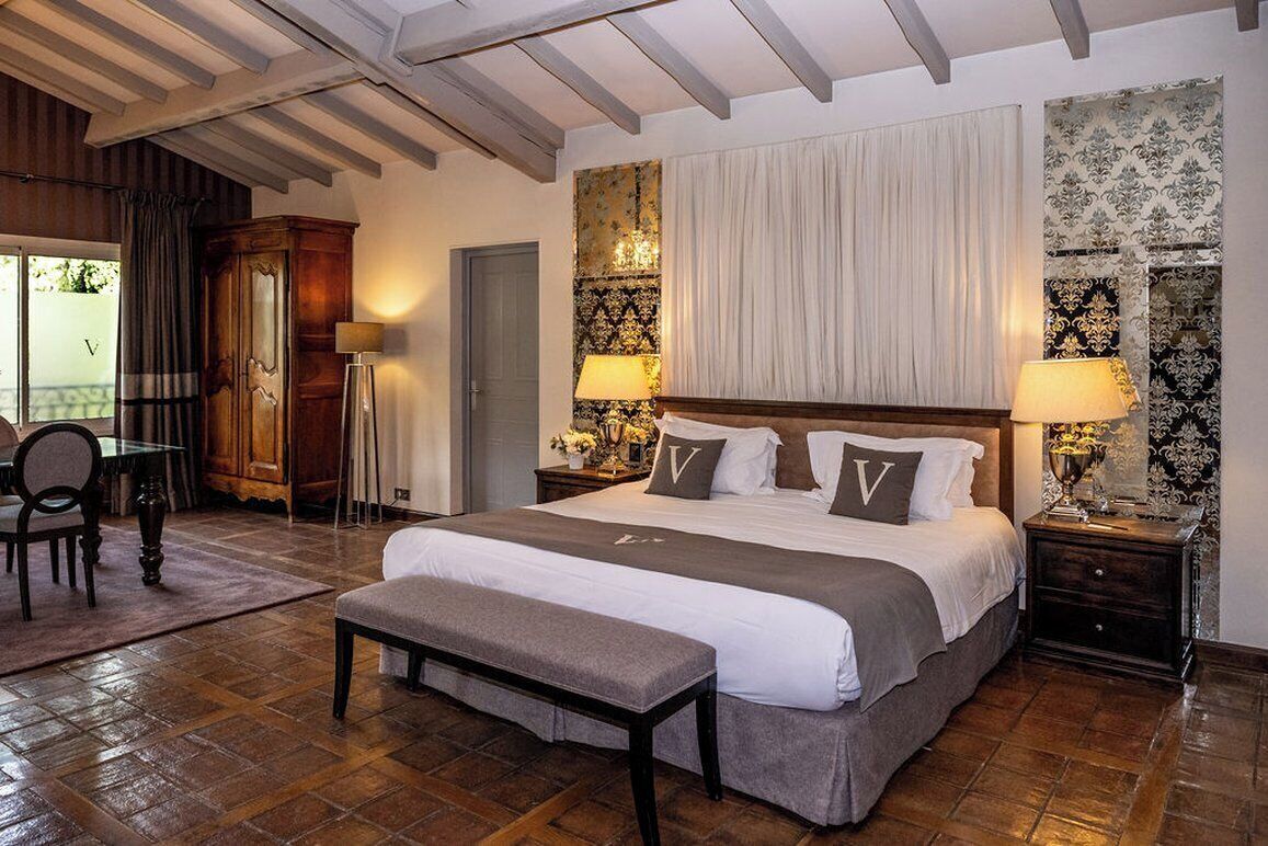 A bedroom with a large bed, two bedside tables with lamps, a bench, a wooden wardrobe, and a chair.