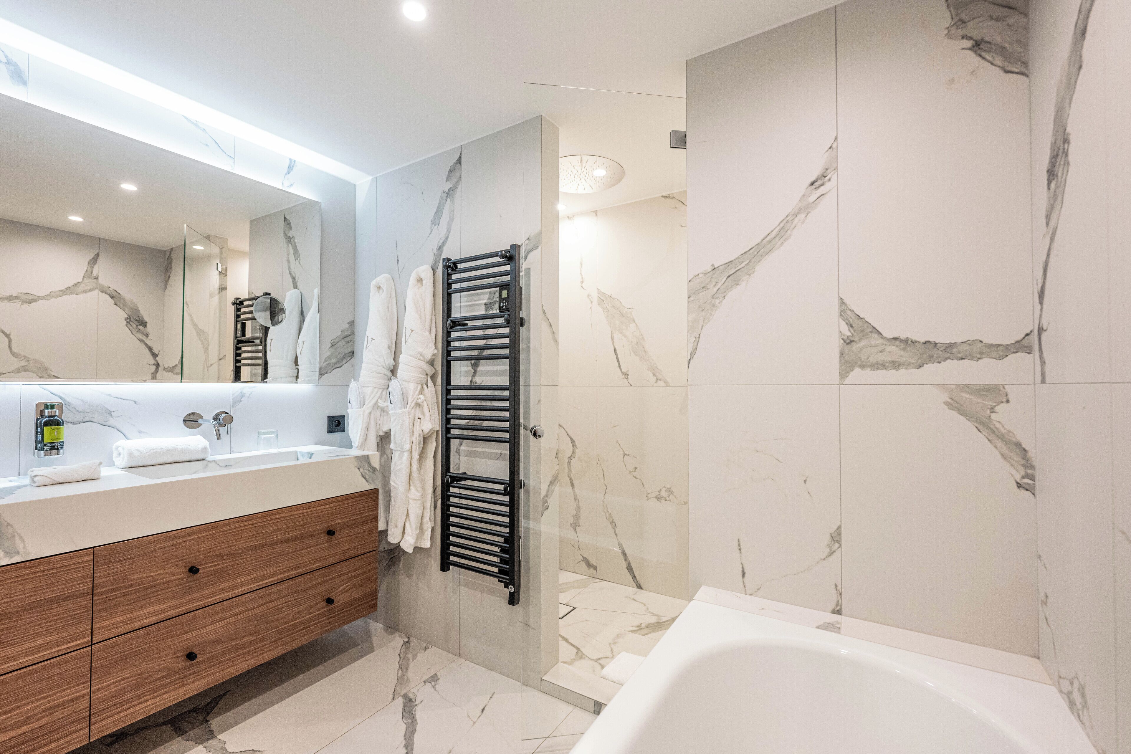 Een moderne badkamer met een marmeren spatwand, een grote spiegel, een houten wastafelmeubel en een bad.