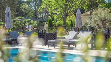 A poolside area with lounge chairs and umbrellas, surrounded by trees and a building in the background.