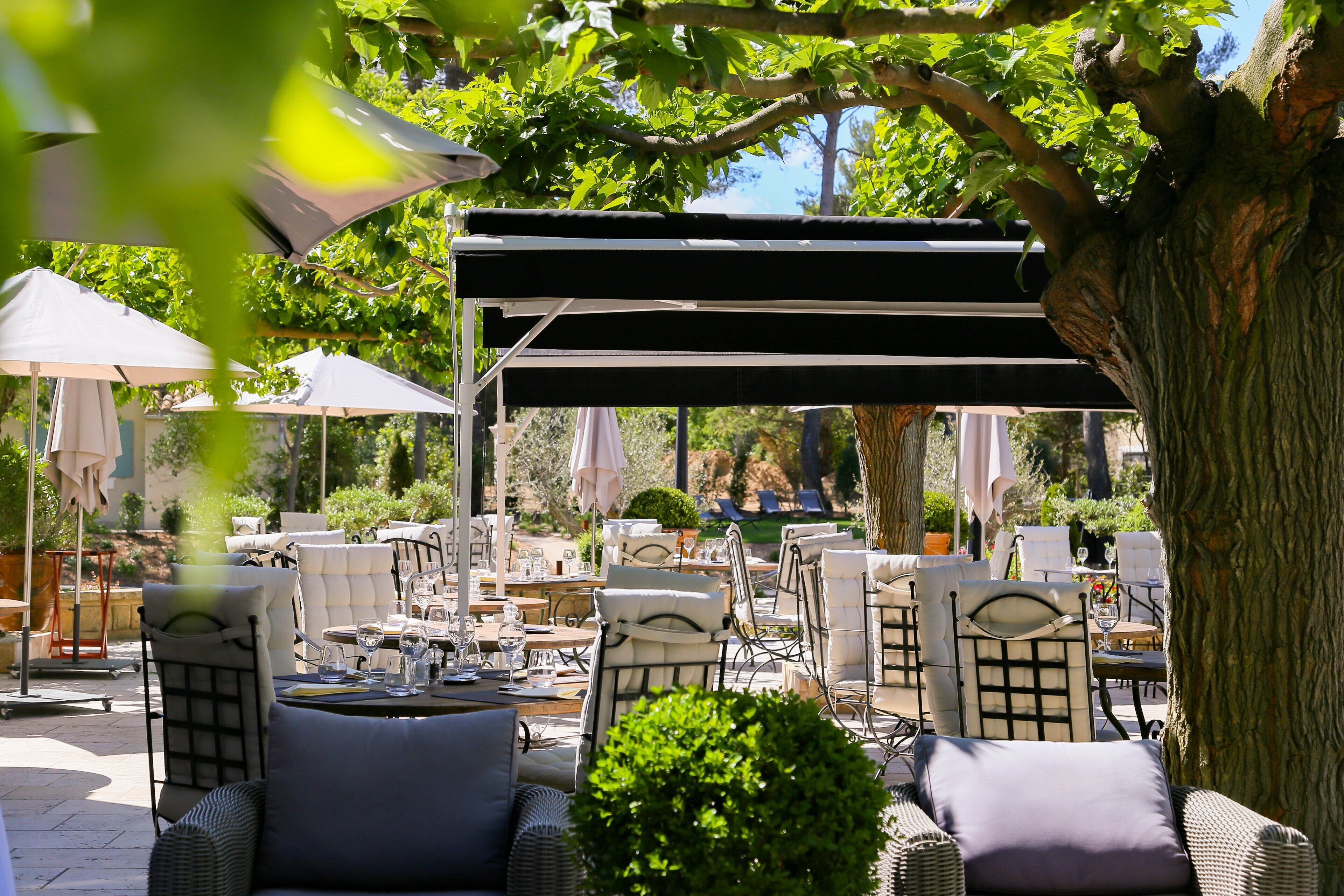 An outdoor seating area with wicker chairs and tables, umbrellas, and a pergola structure.