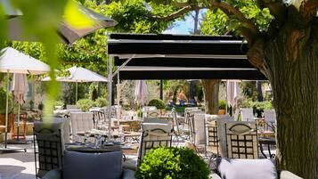 Un espace extérieur aménagé avec des chaises et des tables en osier, des parasols et une structure en forme de pergola.