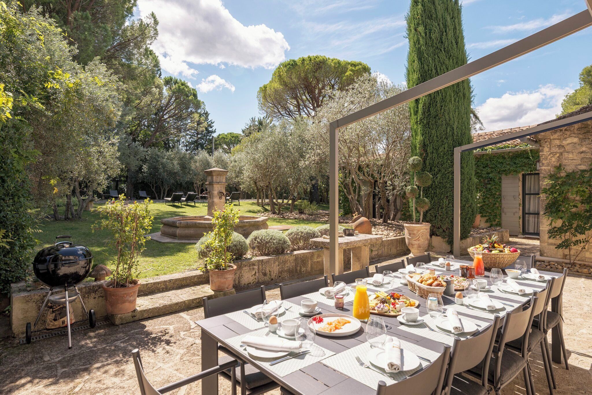 Un espace de restauration en plein air avec une table dressée pour le petit-déjeuner, entouré de plantes en pot et d’un mur de pierres.