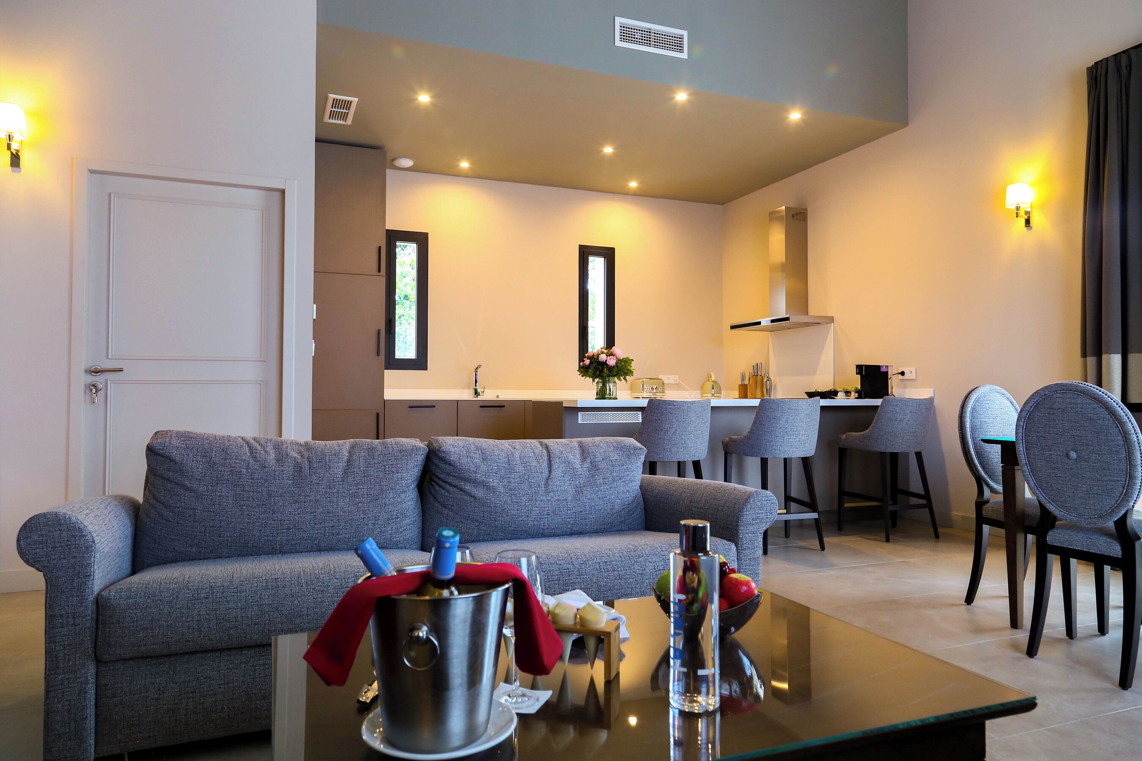 A modern living room with a grey sofa, a coffee table with drinks, and a kitchen area in the background.