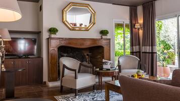 Una sala de estar con chimenea, dos sillones, una mesa de centro, televisor y un ventanal con vistas al verdor.