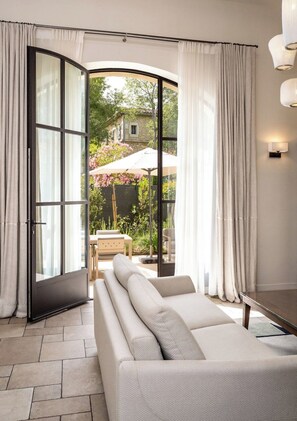 A modern living room with a sofa, a dining table, and a view of a garden through a glass door.