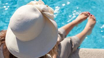 A person relaxing by a pool with a white hat and red nail polish.