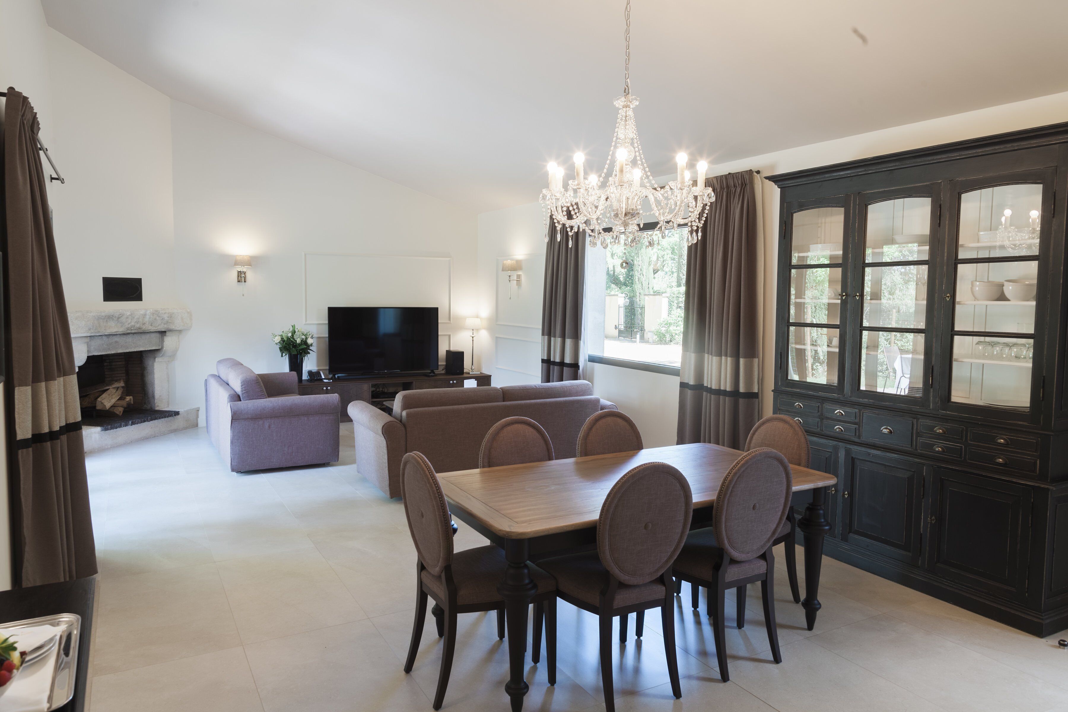 A dining area with a wooden table and chairs, a sofa, a television, and a cabinet with glass doors.