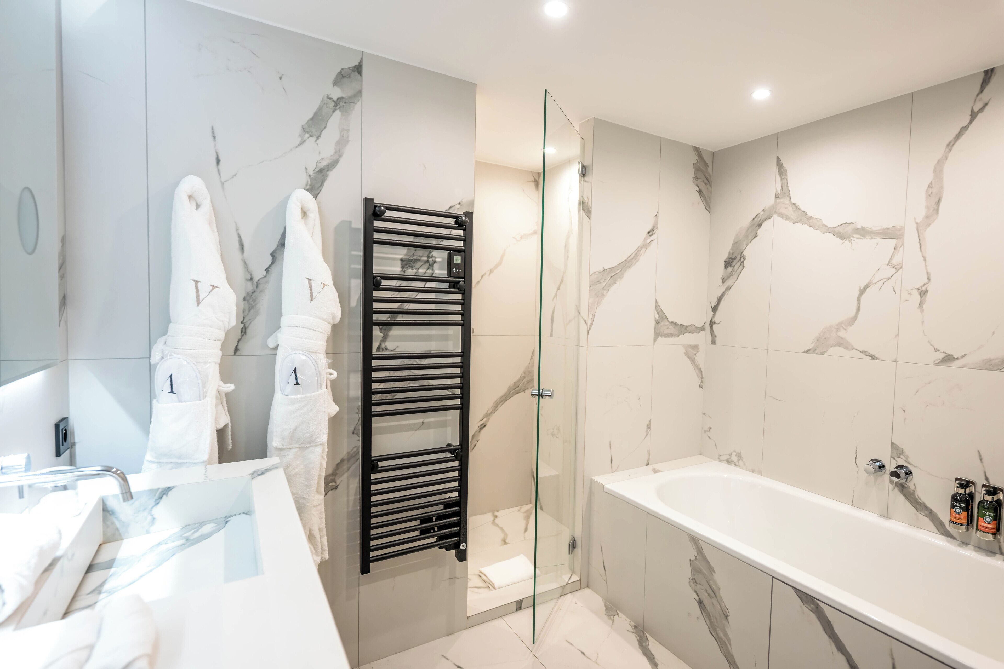 Un baño moderno con ducha de vidrio, bañera blanca y toallero negro.