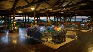 Un espace de détente intérieur aménagé avec des meubles en osier, un plancher en bois et une vue sur l’océan.