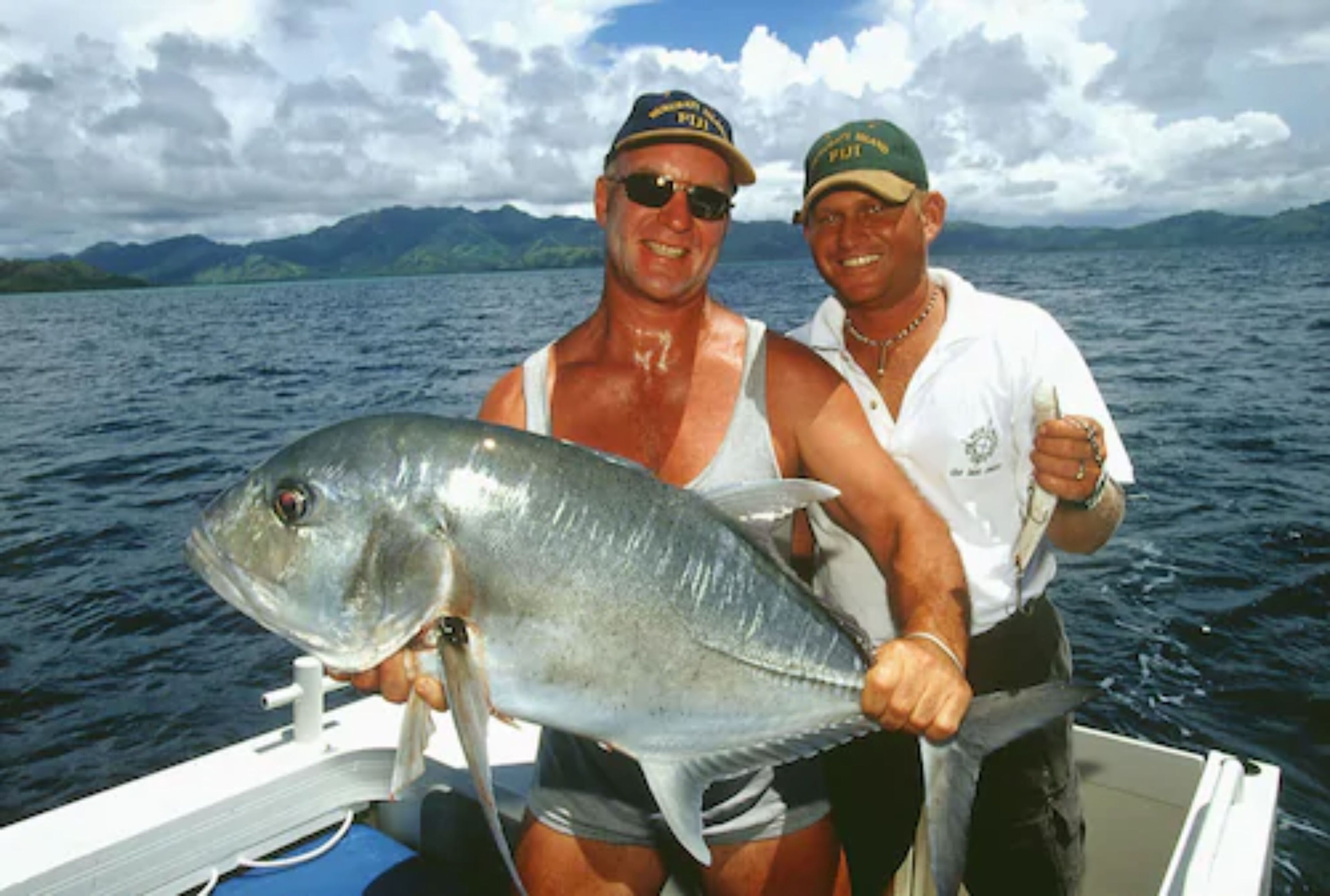 Two people on a boat holding a large fish.