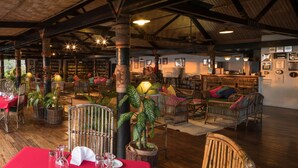 Un restaurant spacieux avec de hauts plafonds, des poutres apparentes, des meubles en osier et différents types de sièges.