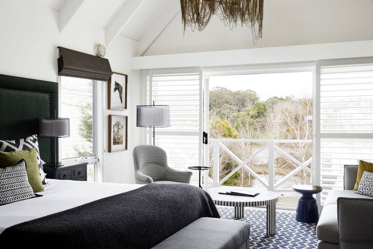 Une chambre d’hôtel moderne dotée d’un grand lit, d’un coin salon avec une table et d’un balcon offrant une vue sur les arbres.