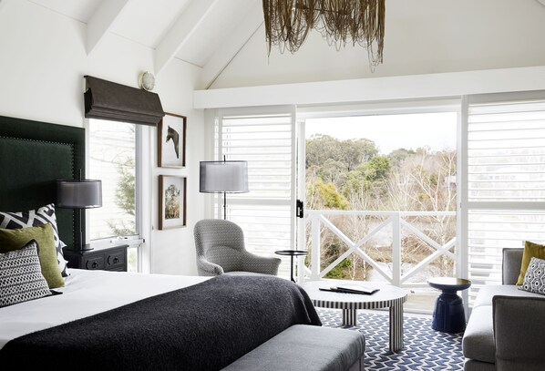 A modern hotel room with a large bed, a seating area with a table, and a balcony with a view of trees. - Lake House Daylesford (Daylesford)
