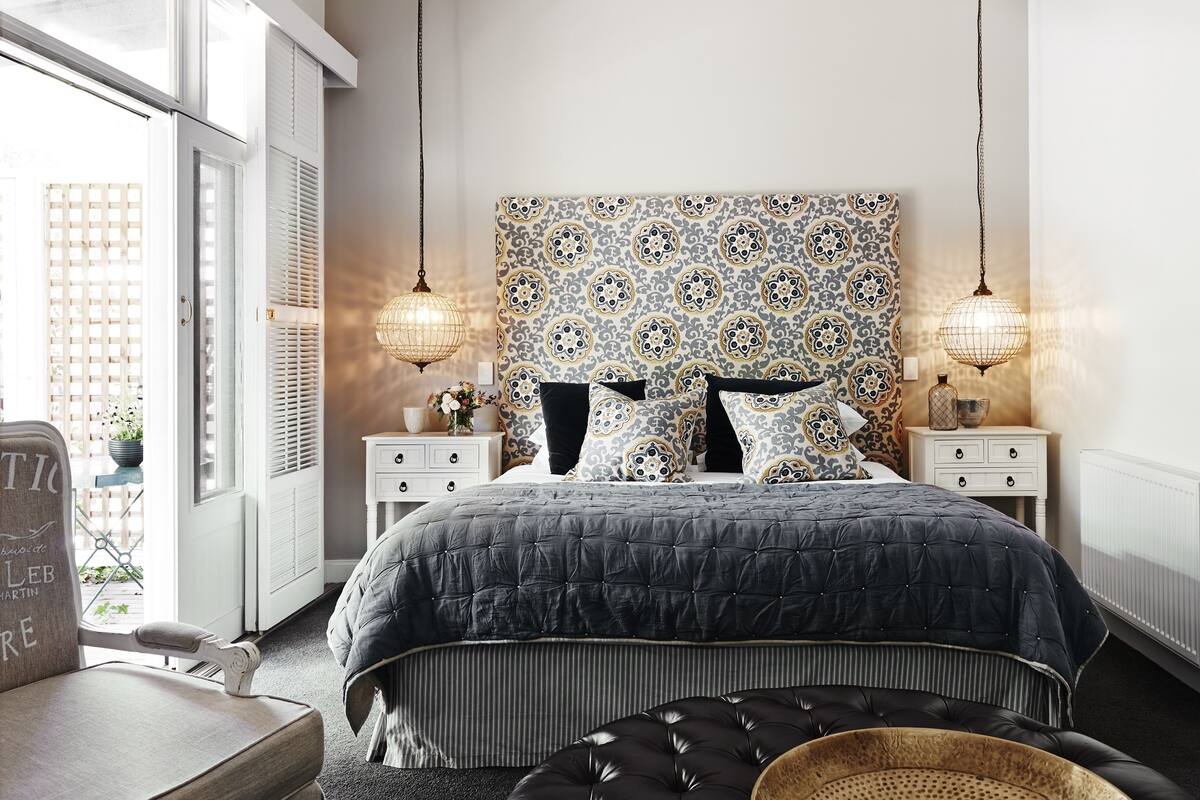 Une chambre avec un grand lit, deux tables de chevet, une tête de lit à motifs et des lampes suspendues.