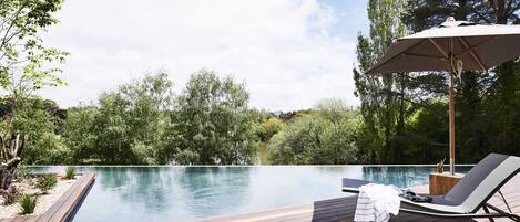 An infinity pool with a wooden deck, a lounge chair, and an umbrella.