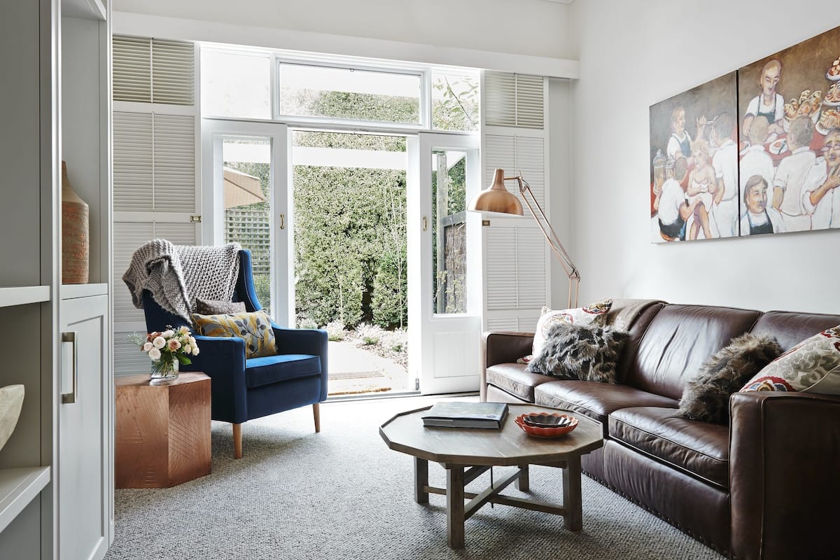Un salon avec un fauteuil bleu, un canapé en cuir marron, une table basse et un tableau accroché au mur.