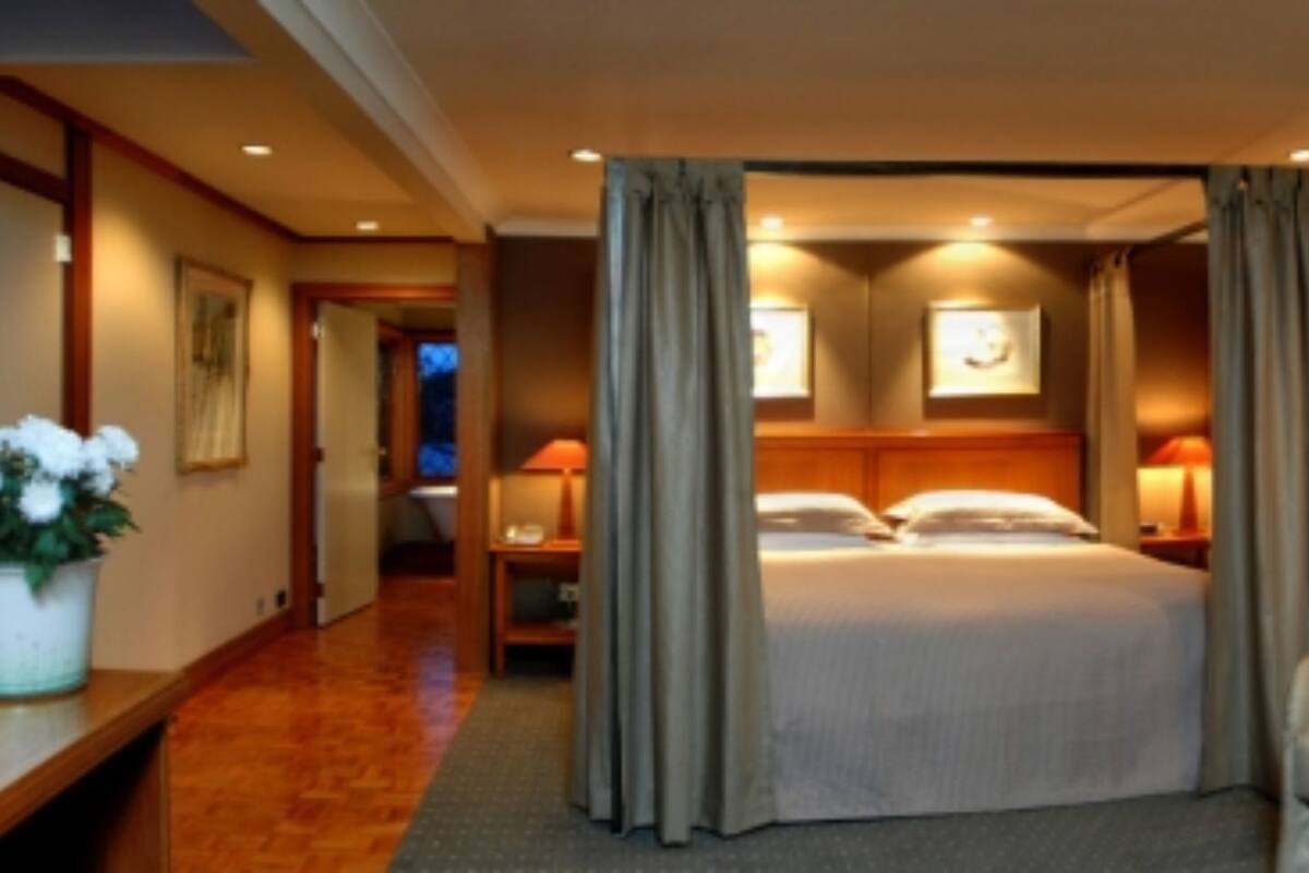 Une chambre d’hôtel avec un lit, deux tables de chevet, une chaise et une grande fenêtre avec des rideaux.