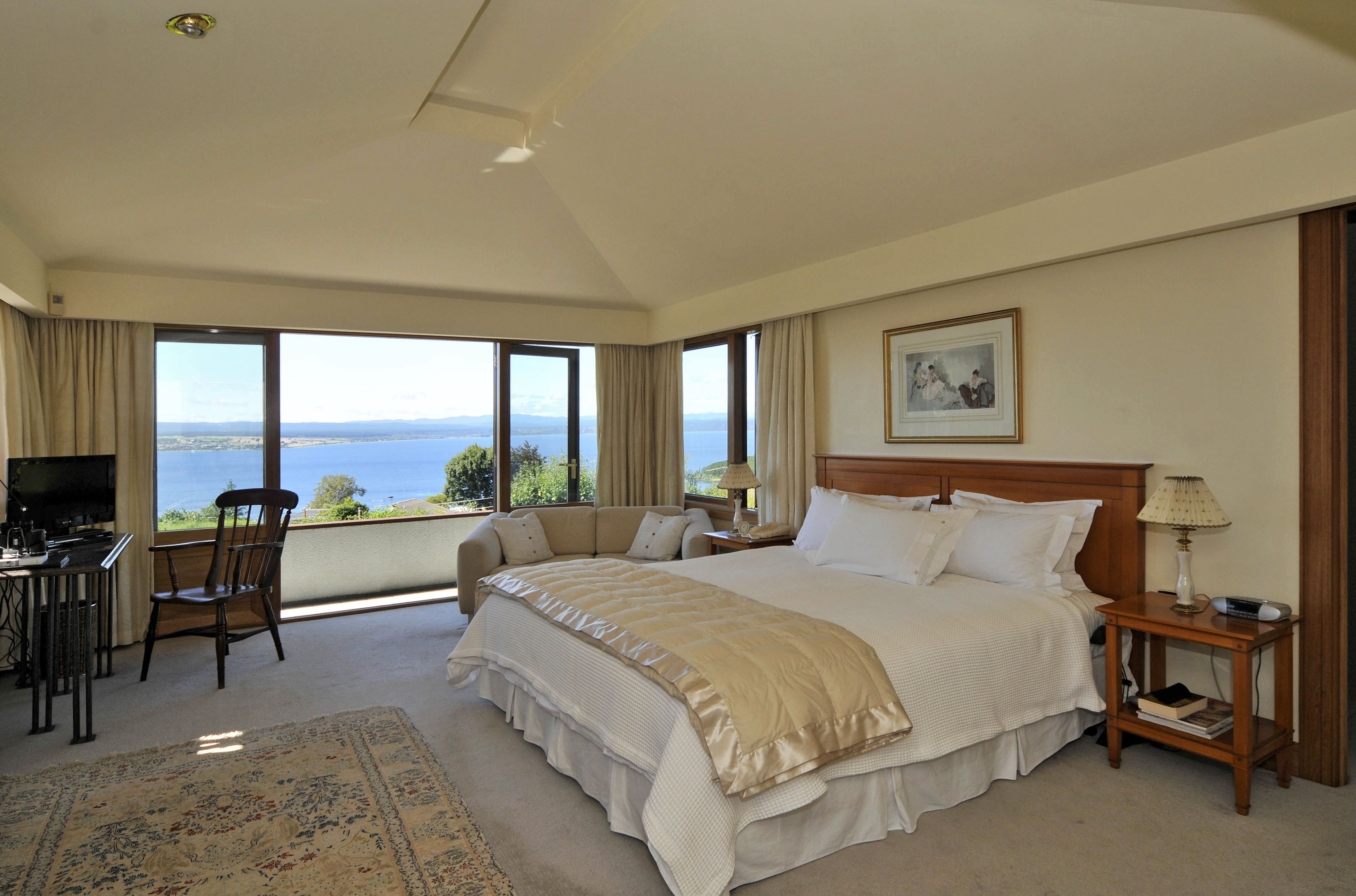 Un dormitorio amplio con una cama grande, un escritorio y una silla. Tiene un ventanal con vistas al mar.