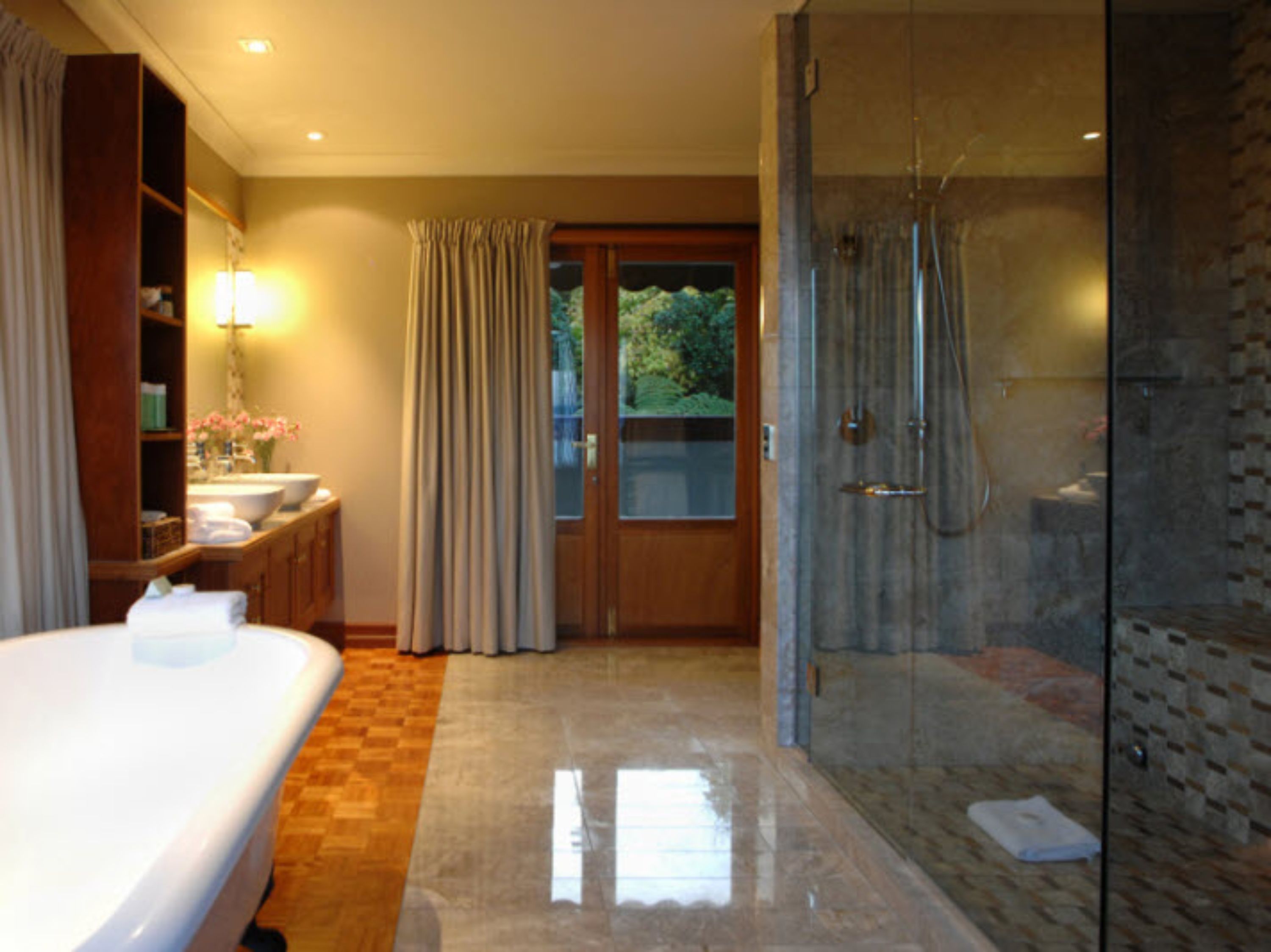 Quarto de hotel com uma cama grande, banheiro com chuveiro e vista para o verde lá fora.