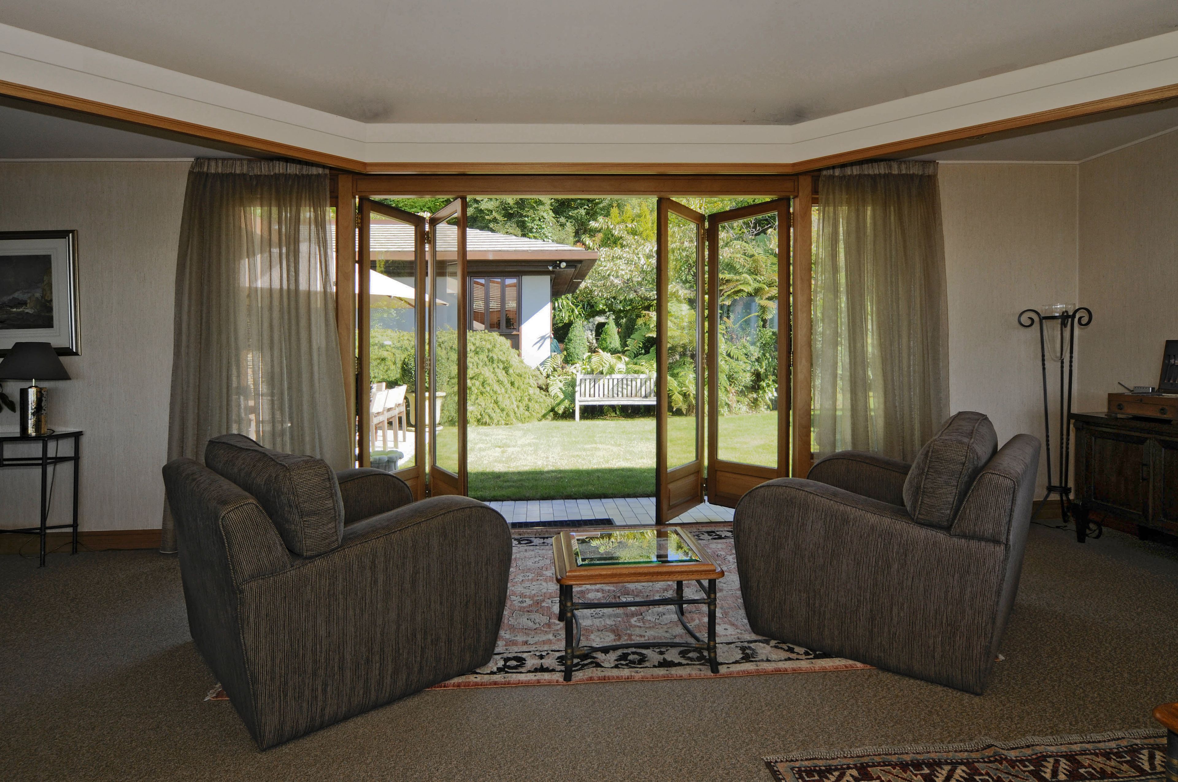 A living room with two armchairs, a glass-top coffee table, and a view of a backyard through a glass door.