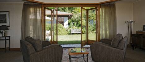 A living room with two armchairs, a glass-top coffee table, and a view of a backyard through a glass door.