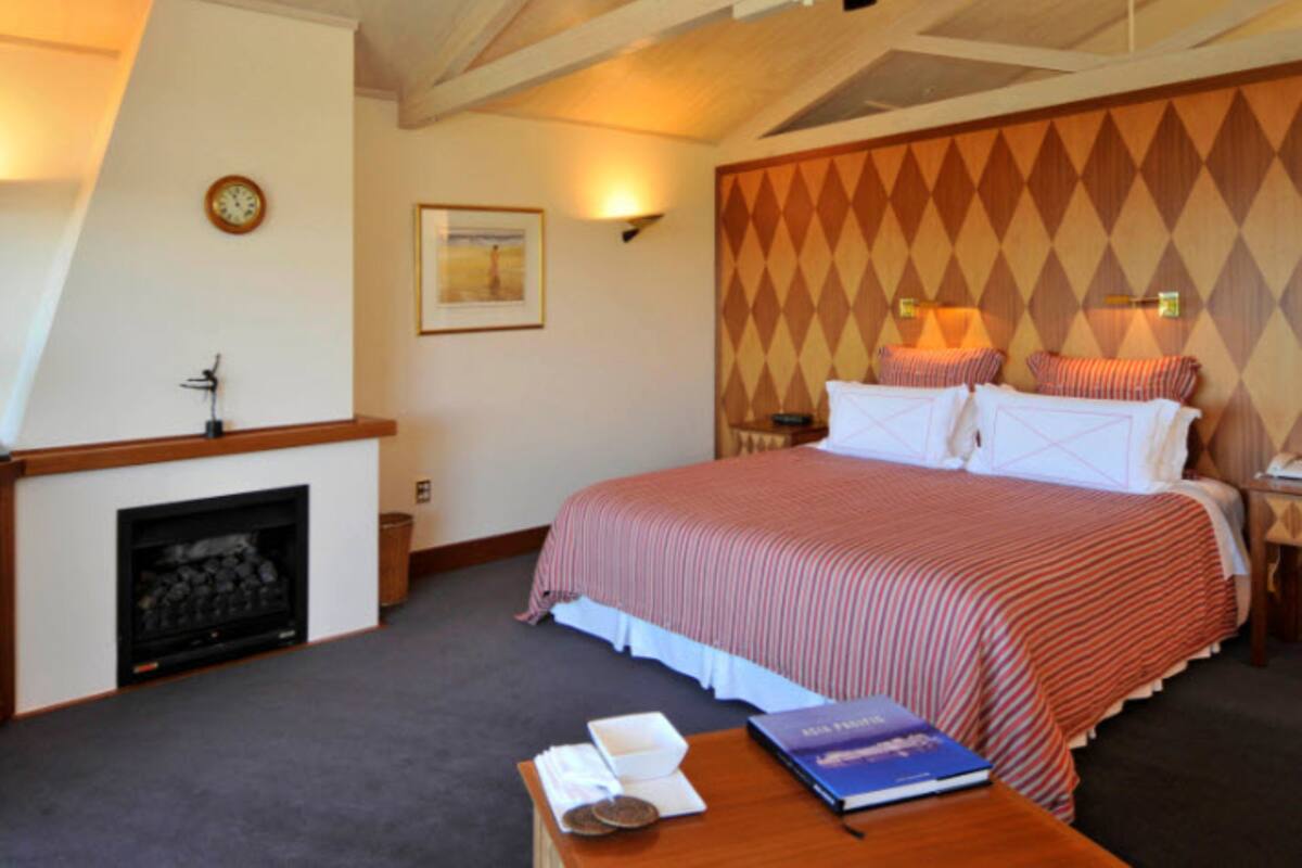 Une chambre d’hôtel avec une cheminée, un lit avec une literie à rayures, une table de chevet et une horloge murale.