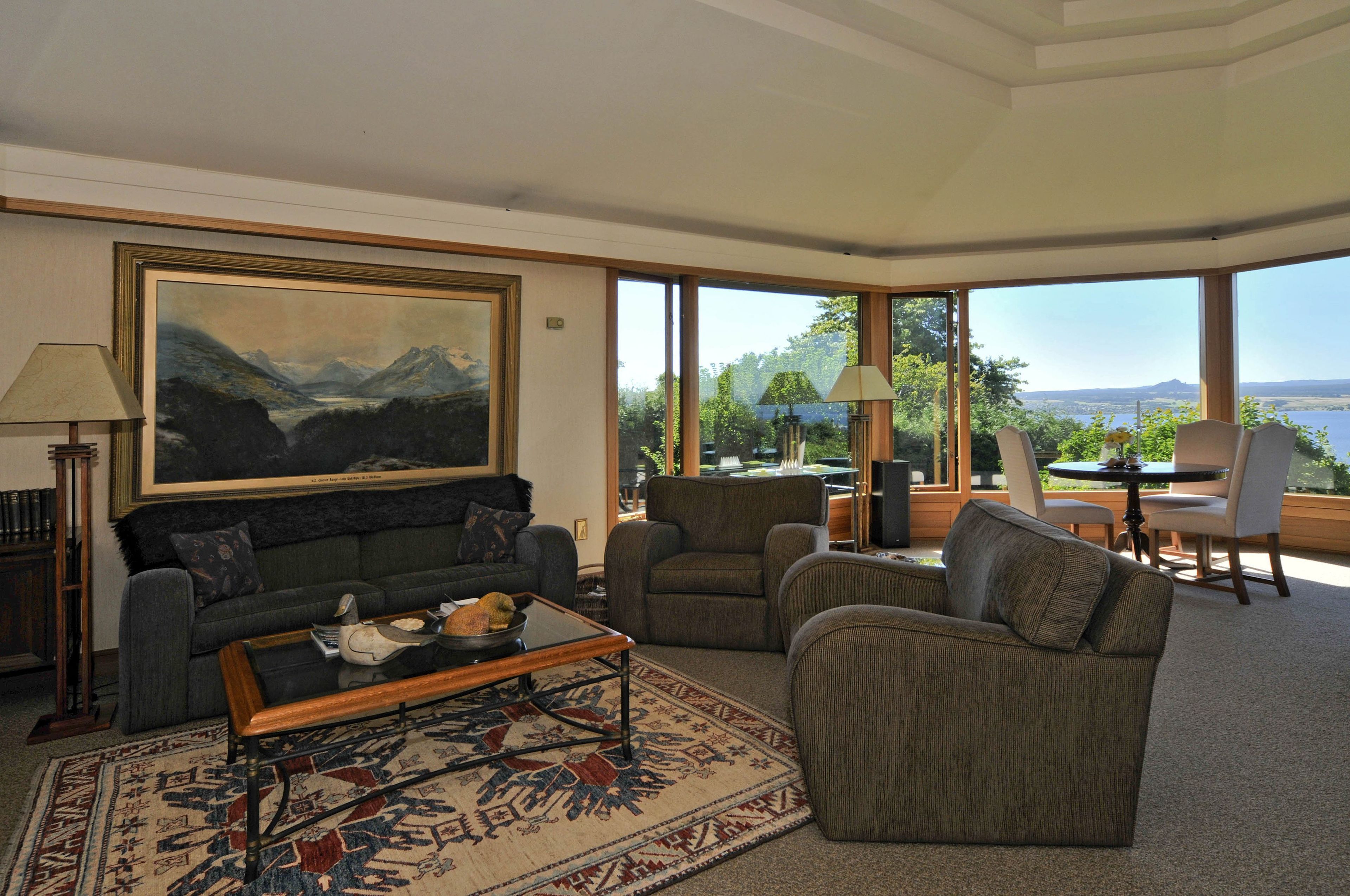 A spacious living room with a large painting, comfortable seating, and a view of the outdoors.