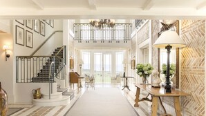 Un vestíbulo espacioso con una imponente escalera, un candelabro y vistas al exterior.