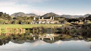 Una casa grande y moderna con un amplio jardín y una masa de agua que refleja la construcción.