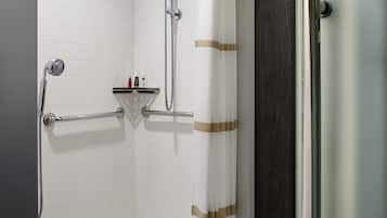 Un baño con paredes de azulejos blancos, una ducha con cabezal de mano, una puerta de ducha de cristal y un perchero con artículos de aseo.