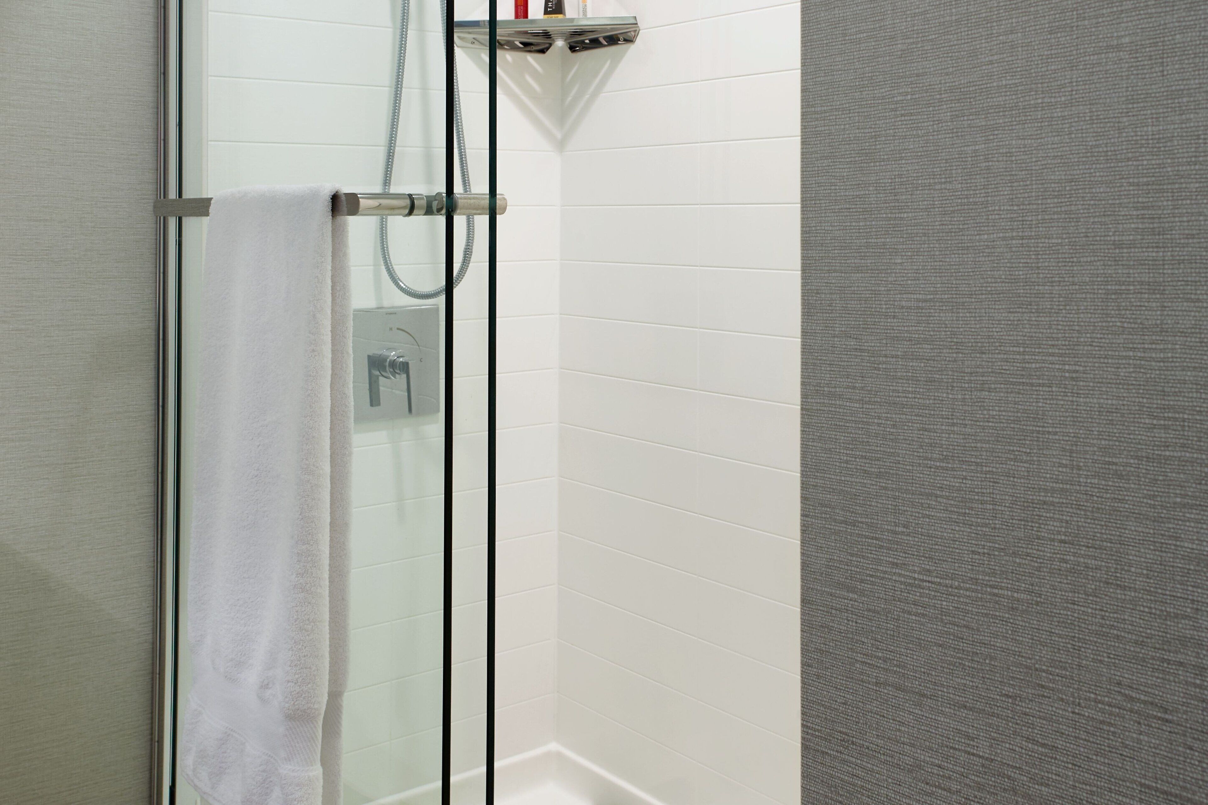 A glass-enclosed shower with a white towel hanging on a metal rack.